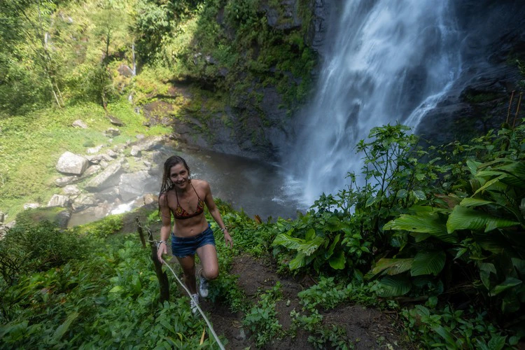 Woman hiking up the trail in front of the esmeralda waterfall in the waterfall valley, colombia.